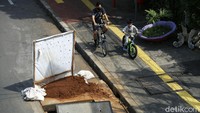 Dua orang pesepeda melintas di samping proyek galian kabel serat optik. 