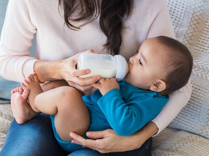 Menyapih Anak Little infant baby lying on mothers hand drinking milk from bottle. Newborn baby drinking milk from bottle. Cute toddler with milk bottle on leg of mother.