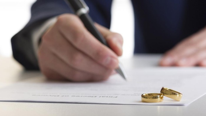 Hands of wife, husband signing decree of divorce, dissolution, canceling marriage, legal separation documents, filing divorce papers or premarital agreement prepared by lawyer. Wedding ring.