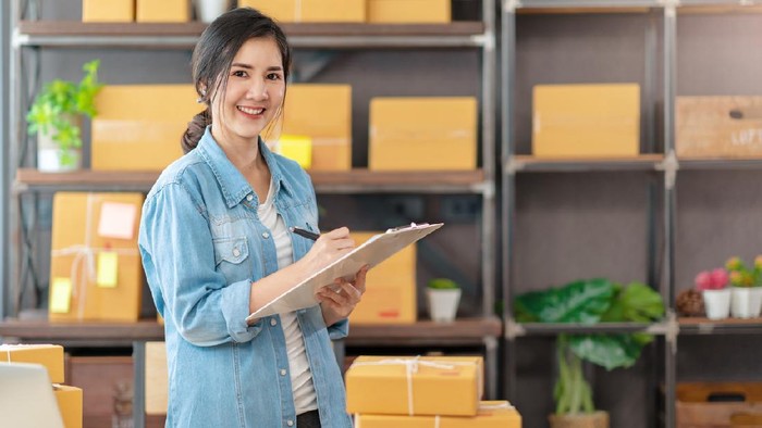Young attractive asian woman owner startup business look at camera work happy with box at home prepare parcel delivery in sme supply chain, procurement, omnichannel or coronavirus quarantine concept.