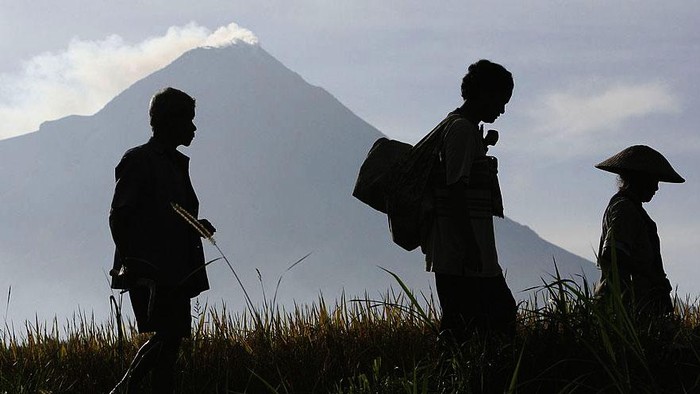 Orang-Orang Tangguh di Seputaran Gunung Merapi YOGYAKARTA, INDONESIA - OCTOBER 29: A man stands in front his house as a Mount Merapi on the backround at Balerante village in Klaten, on October 29, 2010, near Yogyakarta, Indonesia. At least 36 people were killed in earlier eruptions this week, with authorities evacuating villagers within a 10km zone after warning more eruptions are imminent. Mount Merapi, the 'Mountain of Fire' is the most active volcano in Indonesia.