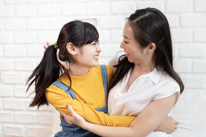 Happy Asian family Mom and teenage daughter embrace together excited, glad in a room that has sunlight from the window at home. Show Love family concept