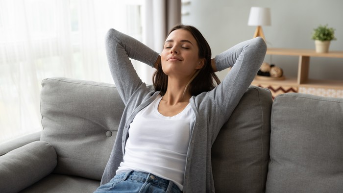 Rileks dan kesehatan mental Relaxed serene pretty young woman feel fatigue lounge on comfortable sofa hands behind head rest at home, happy calm lady dream enjoy wellbeing breathing fresh air in cozy home modern living room