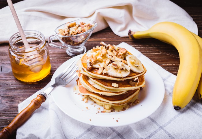Pancakes with banana, walnuts and honey. Healthy breakfast. On dark wooden table background.