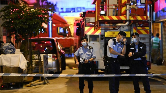 Police officers work next to a firefighter truck at the location of a fire in Hong Kong on early November 16, 2020 where seven people were killed and several others were injured when a blaze tore through an apartment on November 15, 2020, the deadliest fire to hit the finance hub in nearly a decade. (Photo by Peter PARKS / AFP)