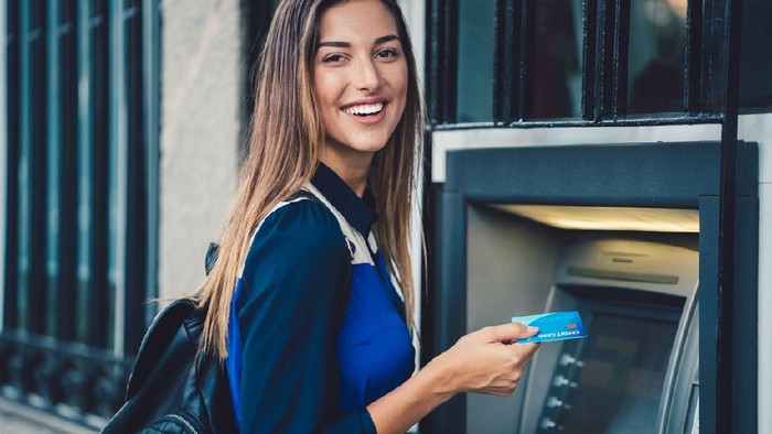Smiling woman at the ATM ready to withdraw cash money   ++++ Note for the inspector: Credit card is fake ++++