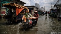 Seorang penjual sayuran mendorong gerobaknya di tengah banjir rob yang merendam kawasan Muara Angke, Jakarta Utara, Senin (16/11/2020).