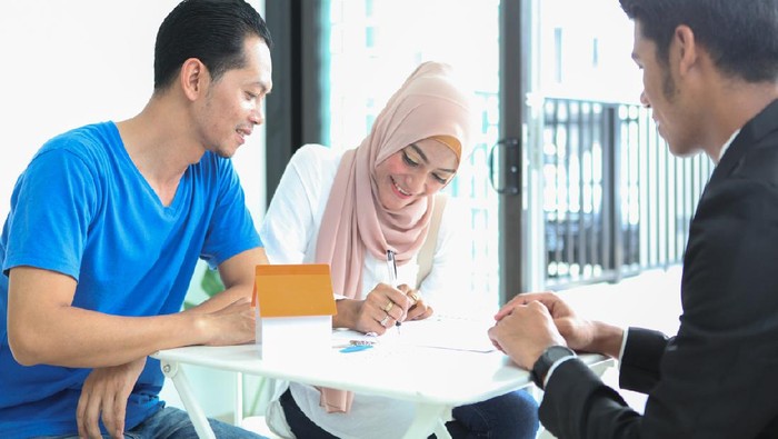 Adult Malay Muslims couple signing documents for house purchase/ rental, sitting in front of a real estate agent.