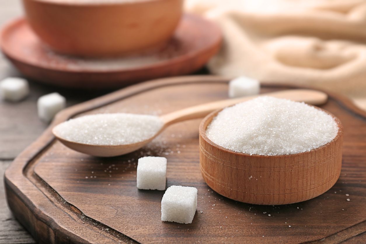 Bowl and spoon with pure sugar on wooden board