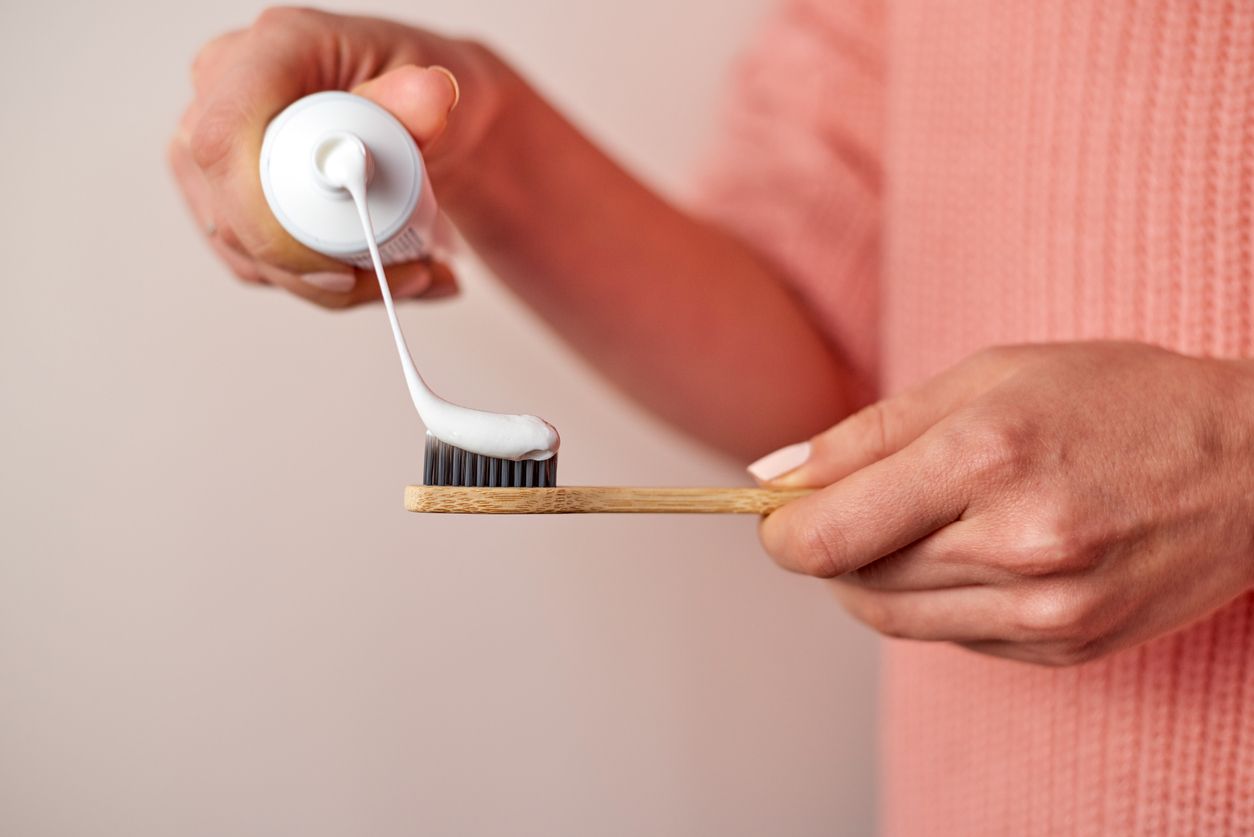 Woman hands squeezing toothpaste on bamboo. Wearing pink knitted sweater