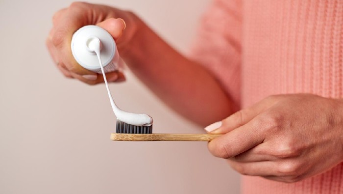 Woman hands squeezing toothpaste on bamboo. Wearing pink knitted sweater