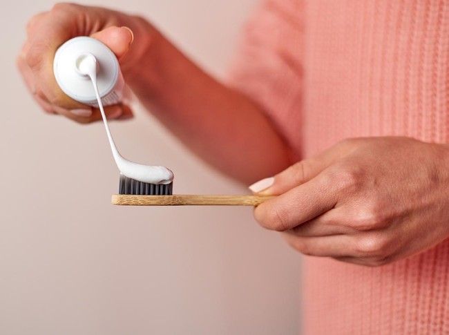 Woman hands squeezing toothpaste on bamboo. Wearing pink knitted sweater