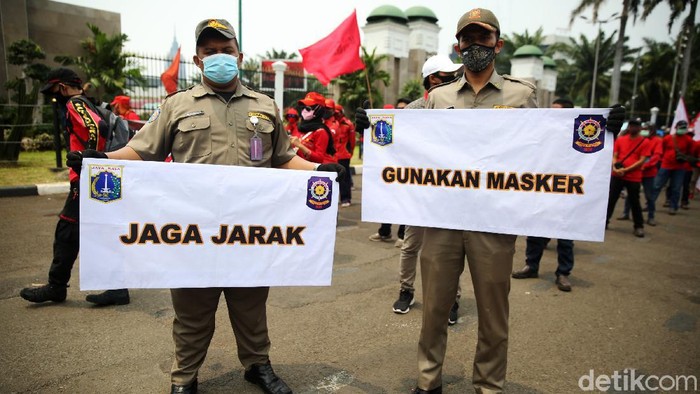 Anggota Satpol PP Kelurahan Gelora mengkampanyekan protokol kesehatan ditengah massa buruh yang demo di depan Gedung DPR, Selasa (17/11/2020). Petugas satpol pp ini mensosialisasikan agar para pendemo menjaga jarak dan memakai masker.