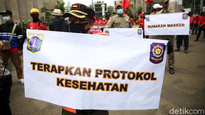 Anggota Satpol PP Kelurahan Gelora mengkampanyekan protokol kesehatan ditengah massa buruh yang demo di depan Gedung DPR, Selasa (17/11/2020). Petugas satpol pp ini mensosialisasikan agar para pendemo menjaga jarak dan memakai masker.