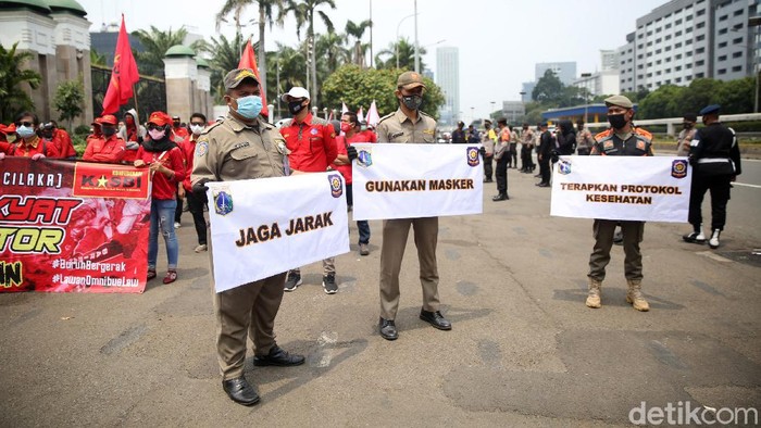 Anggota Satpol PP Kelurahan Gelora mengkampanyekan protokol kesehatan ditengah massa buruh yang demo di depan Gedung DPR, Selasa (17/11/2020). Petugas satpol pp ini mensosialisasikan agar para pendemo menjaga jarak dan memakai masker.