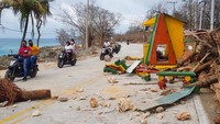 Warga melintas di antara puing-puing dan batang pohon yang rusak diterjang badai.