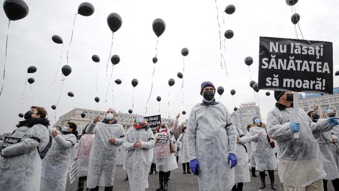 Mengenang Pasien COVID-19 yang Tewas Terbakar di RS Medical workers, wearing masks for protection against the COVID-19 infection, hold black balloons in memory of those who lost their lives while in the care of the state health system in Bucharest, Romania, Tuesday, Nov. 17, 2020. A fire last week at a hospital treating COVID-19 patients in northeastern Romania killed 11 people who were intubated in the intensive care unit. Banner reads