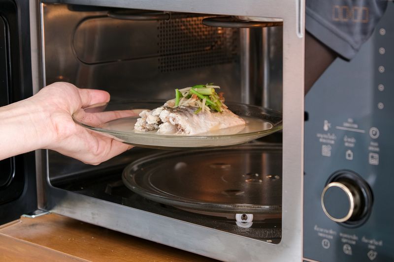 A housewife steaming fish in a microwave oven for a family dinner. She prepares it by putting fish dishes in the microwave and then serving healthy food. Cooking ideas