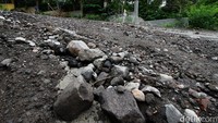 Bebatuan terlihat di sekitar jalan rusak tersebut.