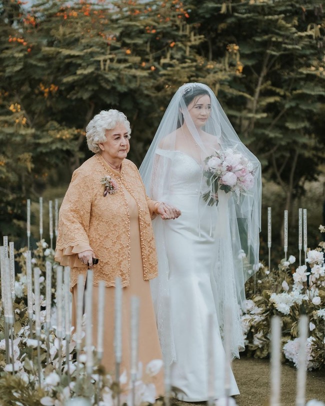 Upacara pernikahan terlihat diadakan di area terbuka atau outdoor. Suasana tampak indah dengan dekorasi mawar putih kreasi Yu Cien Lotus Design. Foto: Instagram/@sumargodeny