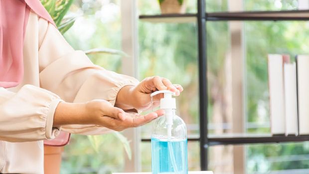 asian muslim woman wear hijab pumping hand sanitizer bottle to wash on desk in office. virus protection concept.