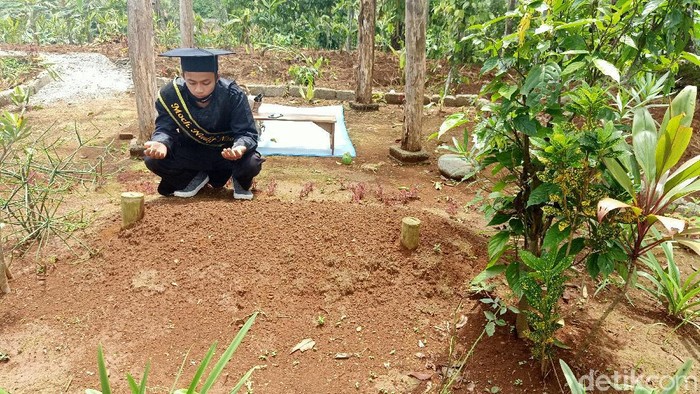 Mochamad Nadif Nasrulloh (23) mengikuti wisuda virtual di depan makam bapaknya, Desa Sidarata, Banjarnegara, Selasa (24/11/2020)