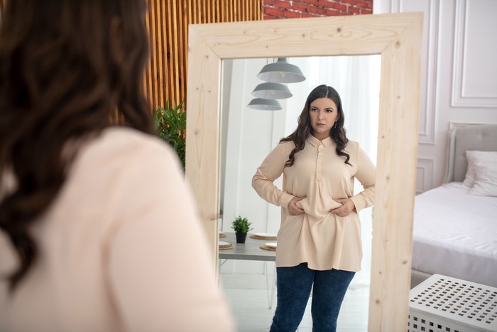 Ilustrasi perut buncit Need to keep a diet. Young woman in a beige blouse touching her belly