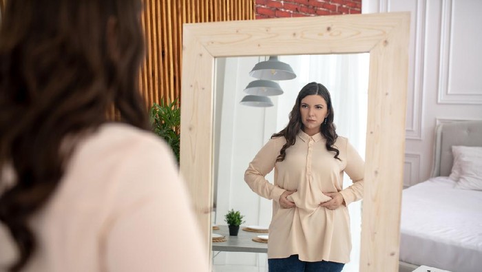 Need to keep a diet. Young woman in a beige blouse touching her belly