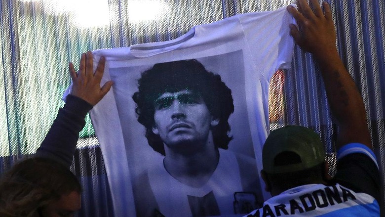 OLIVOS, ARGENTINA - NOVEMBER 03: Fans hold a jersey with the face of Diego Maradona at Clínica Olivos on November 03, 2020 in Olivos, Argentina. Personal doctor of Maradona, Leopoldo Luque, confirmed the former footballer will under a surgery to treat a clot in his brain. Maradona, who turned 60 on Friday 30, had spent the night of Monday hospitalized after being admitted with symptoms of depression. (Photo by Marcos Brindicci/Getty Images)