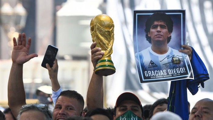 Diego Maradona BUENOS AIRES, ARGENTINA - NOVEMBER 26: A fans holds a photograph of Diego Maradona and a replica of the world cup trophy as he queues to enter the government palace on November 26, 2020 in Buenos Aires, Argentina. Maradona died of a heart attack at his home on Thursday 25 aged 60 . He is considered among the best footballers in history and lead his national team to the World Cup in 1986. President of Argentina Alberto Fernandez declared three days of national mourning. (Photo by Rodrigo Valle/Getty Images)