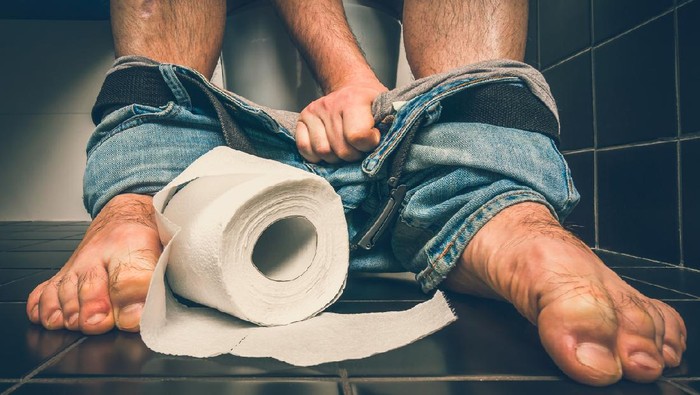 Man suffers from diarrhea is sitting on toilet bowl and toilet paper roll near his legs - diarrhea concept