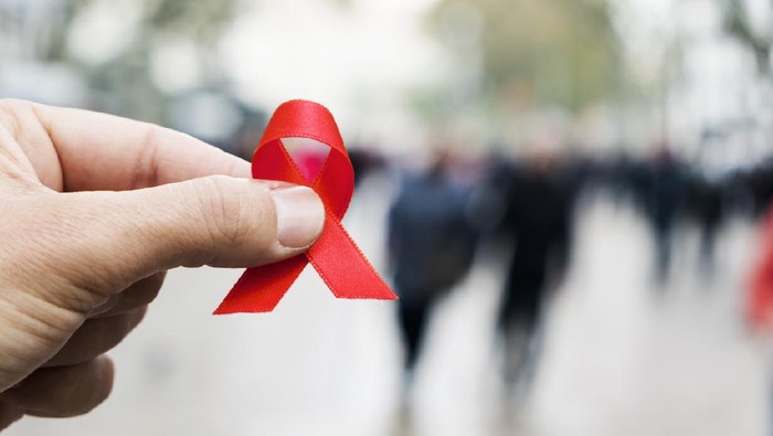 Hari AIDS Sedunia closeup of a red awareness ribbon for the fight against AIDS in the hand of a young caucasian man in a busy pedestrian street of a city
