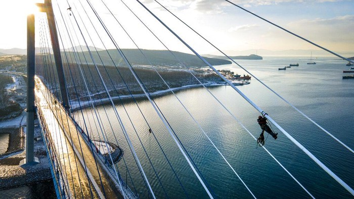 Russia Ice Storm An industrial climber removes ice from the cables of the Russky Bridge across the Eastern Bosphorus Strait in Vladivostok, Russia, Monday, Nov. 30, 2020. The bridge was temporarily closed after an ice storm, with a ferry service launched between Russky Island and mainland Vladivostok. Primorye was hit by freezing rain on Nov. 18. Thick layers of ice covered trees, cars, roads and power lines, many of which broke under the weight. The ice storm continued for several days. (AP Photo/Aleksander Khitrov)