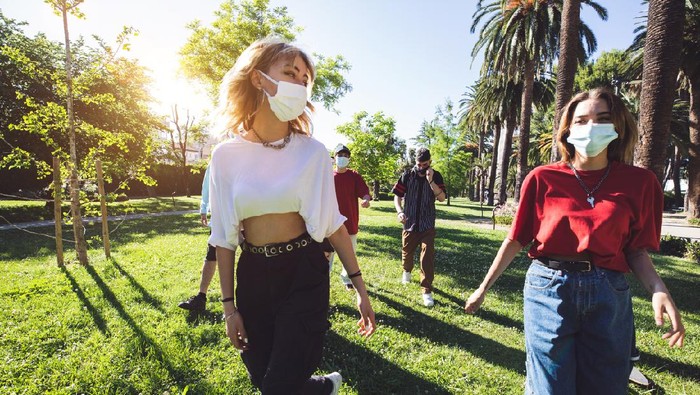 Generation Z teenagers wearing protective face masks and keeping social distancing hanging out together during Covid-19 Coronavirus epidemic spread.