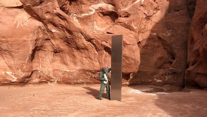 Monolit Misterius Ditemukan di Tengah Gurun FILE - In this Nov. 18, 2020, file photo provided by the Utah Department of Public Safety, a Utah state worker stands next to a metal monolith in the ground in a remote area of red rock in Utah. The mysterious silver monolith that was placed in the Utah desert has disappeared less than 10 days after it was spotted by wildlife biologists performing a helicopter survey of bighorn sheep, federal officials and witnesses said. The Bureau of Land Management said it had received credible reports that the three-sided stainless steel structure was removed on Nov. 27. (Utah Department of Public Safety via AP, File)