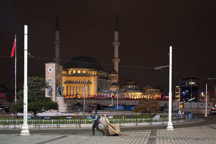 Virus Outbreak Turkey A cardboard collector walks on the iconic Taksim Square, in central Istanbul, deserted during a curfew Tuesday, Dec. 1, 2020, part of the new measures to try curb the spread of the coronavirus. Turkey had gone into the most widespread lockdown so far amid a surge in COVID-19 infections, extending curfews to weeknights and full lockdowns over weekends. The curfew would be implemented on weekdays between 9:00 pm and 5:00 am. He also announced total weekend lockdowns from 9:00 pm on Friday evenings to 5:00 am Monday. (AP Photo)