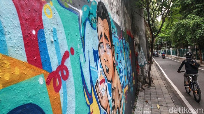 Warga melintas di depan grafiti Tumbang di kawasan Cikini, Jakpus. Tulisan Tumbang dilengkapi mural karakter pria mengenakan baju coklat dengan nametag DKI-1.