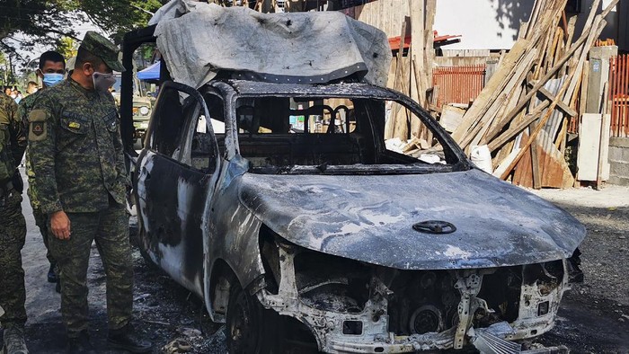 Police wearing to prevent the spread of the coronavirus check a burned patrol car in Datu Piang, Maguindanao province, southern Philippines on Friday Dec. 4, 2020. Dozens of Muslim militants aligned with the Islamic State group opened fire on a Philippine army detachment and burned a police patrol car in a southern town but withdrew after troops returned fire, officials said Friday. (AP Photo/Ferdinandh Cabrera)