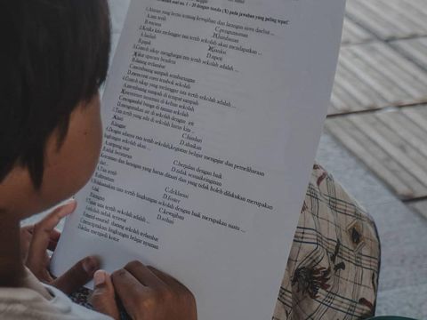Bocah pemulung memegang secarik kertas tugas