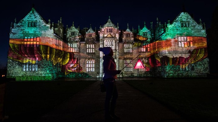 Glow Wild HAYWARDS HEATH, ENGLAND - DECEMBER 03: A woman poses for a photograph in front of an animated projection on the side of Wakehurst House during the launch of