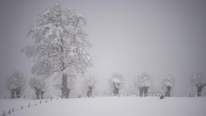 People walk close to an ancient church as the snow covered the landscape in small village of Roncesvalles, northern Spain, Sunday, Dec. 6, 2020. (AP Photo/Alvaro Barrientos)