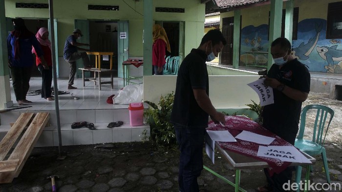 TPS DARURAT BARAK PENGUNGSIAN MERAPI Warga bersama petugas KPPS mempersiapkan TPS darurat untuk Pilkada Kabupaten Sleman di area barak pengungsian balai desa Glagaharjo, Cangkringan, Sleman, Yogyakarta, Selasa (8/12/2020). Komisi Pemilihan Umum (KPU) Kabupaten Sleman memutuskan untuk memindahkan satu buat Tempat Pemungutan Suara (TPS) Padukuhan Kalitengah Lor, Glagaharjo, Cangkringan ke Balai Desa Glagaharjo. Tepatnya di halaman sekolah Tk di dekat barak pengungsian Glagaharjo, Cangkringan, Sleman. Tujuan relokasi TPS adalah agar warga yang dipengungsian tidak perlu kembali ke Kalitengah Lor untuk memilih. Apalagi warga yang berada di pengungsian adalah kelompok rentan yang didominasi lansia. detikcom/Pius Erlangga