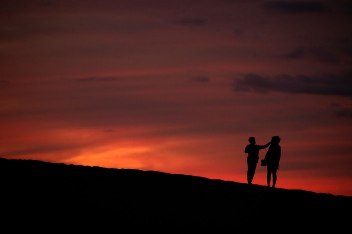 MASPALOMAS, SPAIN - DECEMBER 05: People enjoy the sand dunes at sunset on December 05, 2020 in Maspalomas, Spain. The dunes at Maspalomas have seen a positive transformation during the Coronavirus pandemic due to the lack of tourism on the Island. Conservation efforts over several years to restore the natural habitat have had a boost due to the lack of disturbance, as many of the dunes have regained their shape and height, and vegetation has started to recover. The area which is a site of special scientific interest and a nature reserve is, according to scientists, losing sand at a rate of 45,000 cubic metres per year, and has seen dunes shrinking by several metres over the last 60 years. (Photo by Dan Kitwood/Getty Images)