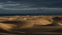 Orang-orang berjalan melalui bukit pasir saat matahari hampir terbenam di Maspalomas, Spanyol.  