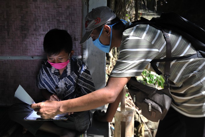 This photo taken on May 20, 2020 shows elementary school teacher Fransiscus Xaverius Fri Harna (R) teaching his student at the students home in Magelang, Central Java, after schools were closed due to the COVID-19 coronavirus outbreak. - Some teachers are taking on dangerous terrain, bad weather and the risk of contracting the COVID-19 coronavirus, to reach home-bound students across the worlds fourth-most populous nation, home to a quarter of billion people. (Photo by AGUNG SUPRIYANTO / AFP) / TO GO WITH Health-virus-Indonesia-education-teaching,FOCUS by Agnes ANYA