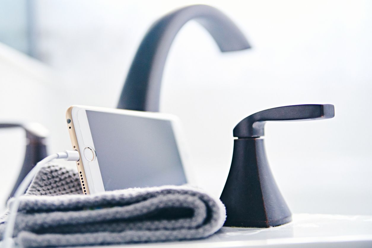 Charging iPhone Peyton, Colorado, USA - March 22, 2018: An iPhone 6s Plus plugged in to a charging cable rests on a clean washcloth next to the faucet on the side of a bathtub.