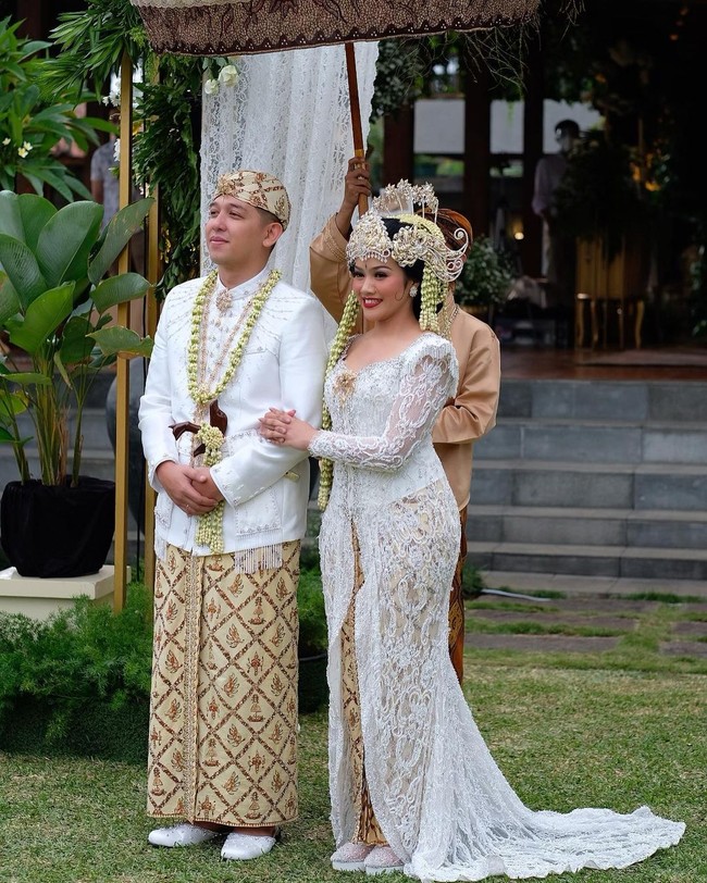 Pernikahan Yura Yunita dan Donne Maulana berlangsung di Cimahi, Jawa Barat, pada Jumat (11/12/2020).Pelantun Cinta dan Rahasia ini membungkus tubuhnya dengan kebaya dari Ayung Berinda Wedding Gallery. Kebaya putih tersebut hadir dengan aksen padding yang dihiasi fringe sehingga meninggalkan kesan mewah. (Foto: Instagram/@ayungberinda)