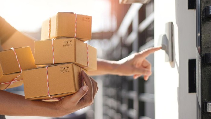 Delivery man holding parcel boxes and ring the doorbell on the clients door in the morning background.