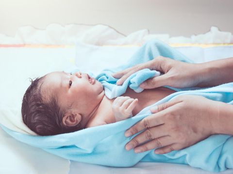 Cute newborn baby girl in towel after bath with mother hands rub her body dry with tenderness