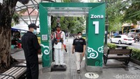 Petugas memantau warga yang melintas di gerbang detektor suhu.
